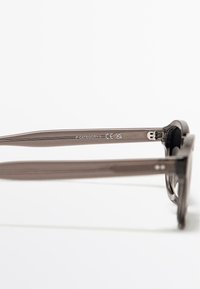 Hnědé plastové sluneční brýle s hladkým povrchem, širokými stranicemi a kovovými doplňky na pantách. Kategorie 3 UV ochrany uvedená na stranicích.