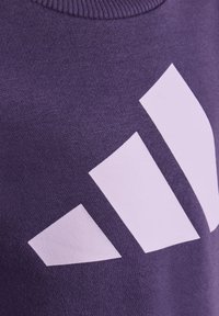 Lila sweatshirt av mjukt tyg, med en stor vit tre-stripes-logotyp som är placerad framträdande på framsidan.