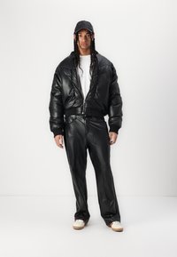 Schwarze gepolsterte Lederbomberjacke mit gerippten Bündchen, kombiniert mit passenden taillierten Lederhosen und weißen Sneakers mit einer leichten Sohle.