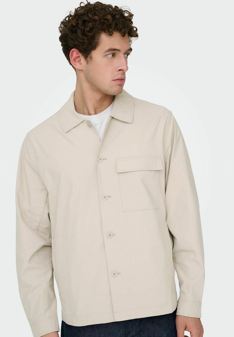 Veste beige à boutons avec col, comprenant une poche poitrine et une texture de tissu lisse. Manches longues et coupe droite.