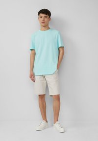 Lichtblauw katoenen T-shirt met korte mouwen, gecombineerd met beige shorts en witte sneakers; eenvoudig ontwerp, relaxte pasvorm, casual uitstraling.