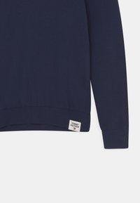Marinblå långärmad tröja med ribbade ärmslut och nederkant, med en liten Tommy Hilfiger logopatch nära nederkanten.