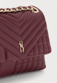 Sac à main en cuir matelassé bordeaux avec un motif en chevron, une bandoulière en chaîne dorée et un logo remarquable sur le devant.