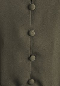 Gros plan sur un tissu vert olive avec quatre boutons ronds recouverts de tissu cousus verticalement en ligne droite.