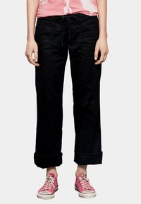 Zwarte, losse broek met een trekkoord in de taille en omgerolde zoom, gemaakt van zachte stof, gecombineerd met roze sneakers.