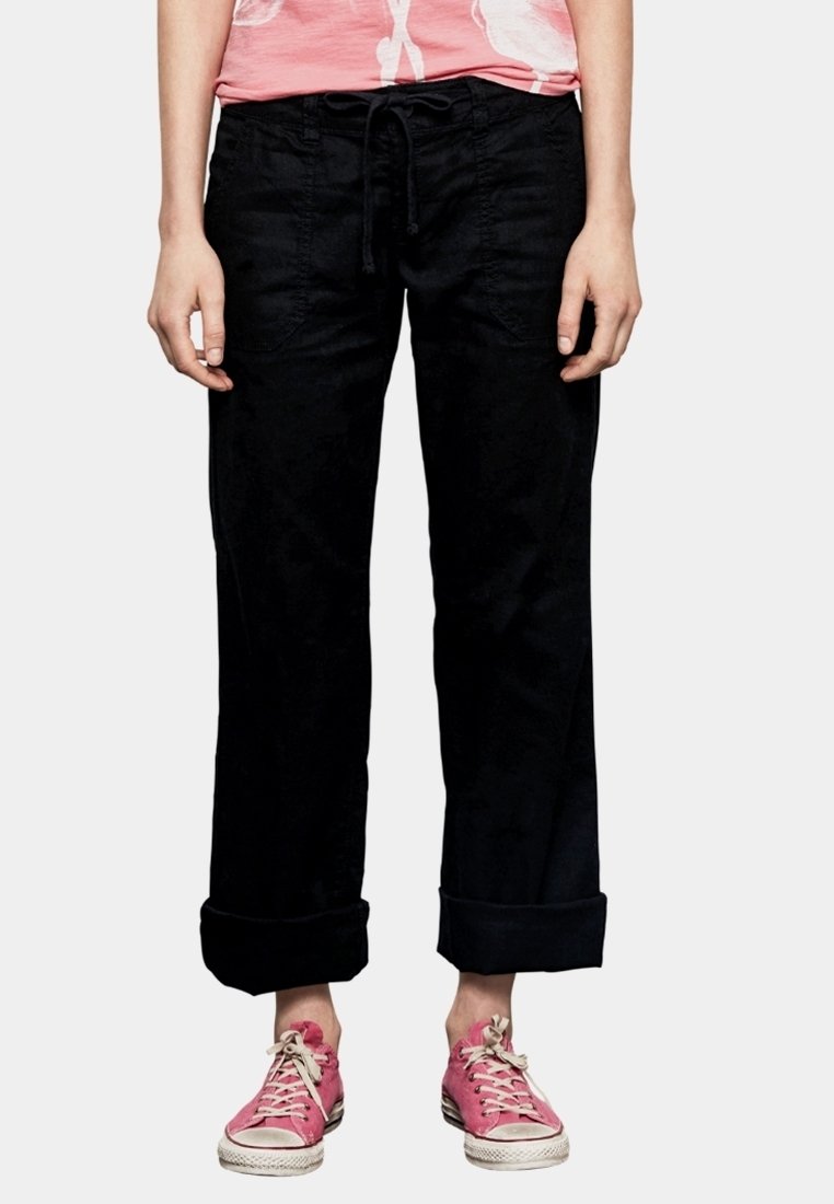 Zwarte, losse broek met een trekkoord in de taille en omgerolde zoom, gemaakt van zachte stof, gecombineerd met roze sneakers.