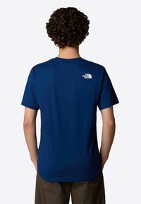 Camiseta de algodón azul con cuello redondo y mangas cortas. Presenta un logo blanco en la parte superior de la espalda. Textura suave, corte estándar.