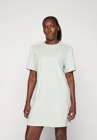 Robe en coton vert clair avec des manches courtes, un col rond et un logo Adidas blanc ; design simple avec des rayures latérales contrastantes.