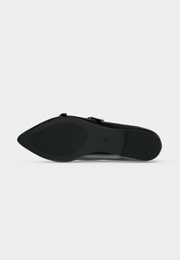 Semelle de chaussure plate noire à bout pointu avec une prise texturée et la taille 37 visible, présentée sur un fond clair uni.