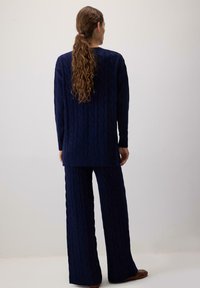 Jūras spēku krāsas adīts džemperis un atbilstoši platās bikses. Tekstūrēts audums ar ribotām piedurknēm un apakšmalu. Apģērbs ir brīva piegriezuma un ērts.