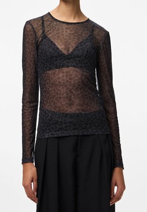 Czarna przezroczysta bluzka z długim rękawem w panterkę, noszona na czarnym bralecie, zestawiona z czarnymi plisowanymi spodniami z wysokim stanem.