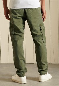 Grønne cargo-bukser med sidelommer, afslappet pasform og manchetter; lavet af blødt, let struktureret stof; parret med hvide sneakers.