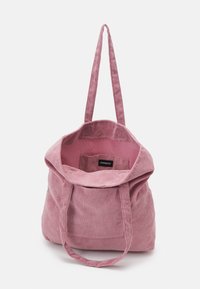 Sac cabas en velours côtelé rose avec deux longues anses et un dessus ouvert montrant une petite poche intérieure et une étiquette de marque à l'intérieur.