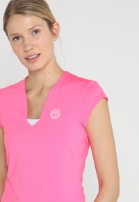 Top atletico rosa con maniche a cappuccio, scollatura a V e un piccolo logo sulla parte sinistra del petto. Realizzato in tessuto liscio ed elasticizzato.