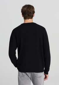 Felpa nera con collo a giro, maniche lunghe, realizzata in tessuto morbido e dalla vestibilità rilassata. Il retro presenta un design semplice, senza loghi o motivi visibili.