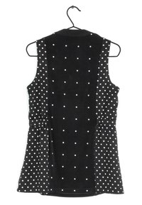 Top senza maniche nero con pois bianchi, dotato di collo a camicia e dettagli arricciati in vita. Appeso a un gancio nero.