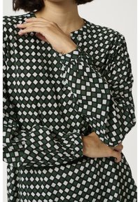 Grüne gemusterte Bluse mit einem Diamantdesign in Weiß, rundem Ausschnitt, Knopfdetails und gerafften Ärmeln mit einer glatten Textur.