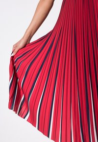 Robe plissée rouge avec des rayures verticales bleu marine et blanches. Le tissu semble lisse et léger, tombant gracieusement d'un haut ajusté.