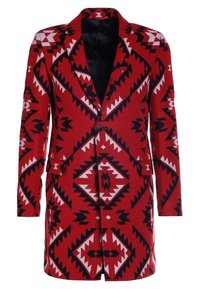 Blazer à motif rouge présentant des dessins géométriques en noir et blanc, fermeture à un bouton, revers crantés et poches latérales.