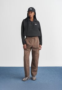 Felpa nera in pile con zip a un quarto, pantaloni cargo beige, scarpe da ginnastica grigie, cappellino nero; texture liscia, vestibilità comoda e colori a contrasto.