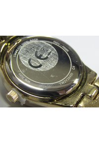 Gouden polshorloge met een roestvrijstalen achterkant, gedetailleerde gravures en een gestructureerd oppervlak, met een kroon aan de zijkant.