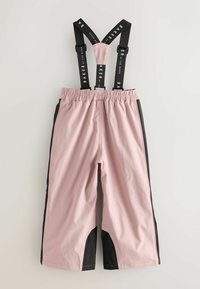 Rožinės vandeniui atsparios kombinezono kelnės su juodomis šoninėmis juostomis, elastingu juosmeniu ir reguliuojamomis juodomis petnešomis, ant kurių yra balti tekstai.