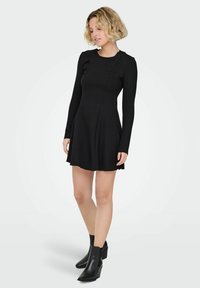 Czarna sukienka z długim rękawem, dopasowaną górą i rozkloszowanym dołem. Wykonana z miękkiego materiału, z detalami szwów i okrągłym dekoltem.