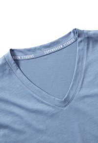 Light blue V-neck T-shirt made of soft fabric, featuring a smooth texture and a neckline label with "Copenhagen Studios" printed.
