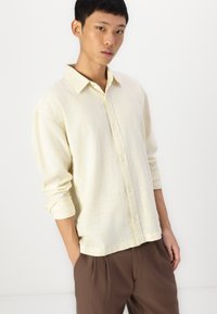 Light yellow button-up shirt made of a textured material with a relaxed fit, featuring a classic collar and rolled sleeves.