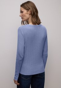 Maglione a maniche lunghe azzurro chiaro a coste con scollo rotondo, orlo dritto e maniche aderenti, indossato con jeans scuri.
