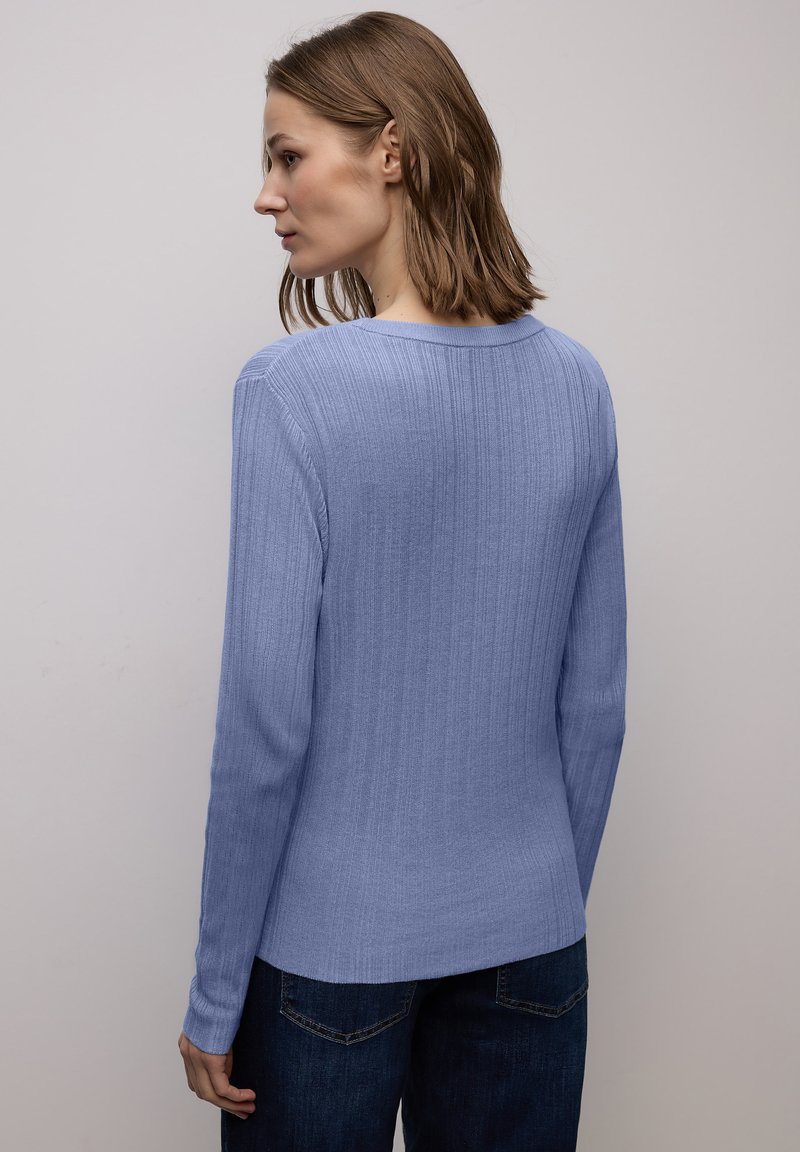 Maglione a maniche lunghe azzurro chiaro a coste con scollo rotondo, orlo dritto e maniche aderenti, indossato con jeans scuri.
