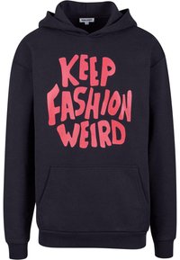 Felpa nera con tasca frontale e cappuccio regolabile. Presenta un audace testo rosa brillante che dice "KEEP FASHION WEIRD" in un font giocoso.