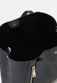 Sac fourre-tout en cuir noir avec un extérieur texturé, des ferrures en or et une ouverture sur le dessus. L'intérieur présente une doublure douce de couleur sombre et un compartiment zippé.