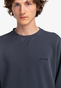 Felpa blu navy con collo a costine e dettaglio a V, caratterizzata da un logo "element" in rilievo sul lato sinistro del petto. Morbida al tatto.