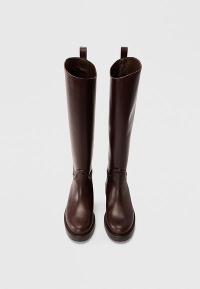 Bottes montantes en cuir marron foncé avec une finition lisse, bout arrondi, semelle plate et languettes en haut pour un enfilage facile.