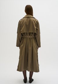 Cappotto trench color khaki con vita cintrata, spalline sulle spalle e tessuto morbido con una silhouette fluida. La vista posteriore mette in evidenza le maniche lunghe.
