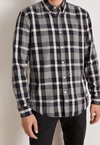 Košile s knoflíky, s černobílým kostkovaným vzorem, s límečkem, dlouhými rukávy a zakřiveným lemem. Látka se zdá být hladká.