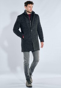 Mantel aus Wollmischung in dunkelgrauem Fischgrätmuster, mit Knopfleiste, hohem Kragen und seitlichen Taschen, kombiniert mit schlanken grauen Hosen und Stiefeln.