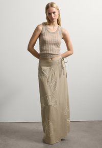 Top de tirantes de punto beige con textura acanalada, combinado con una falda larga de estilo envolvente que presenta patrones bordados en hojas de ginkgo blancas.