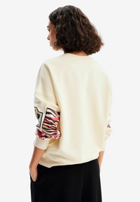 Felpa color crema con maniche oversize caratterizzata da un audace motivo a strisce di tigre rosso e nero e polsini a coste.