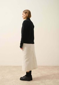 Czarny dzianinowy sweter, kremowa długa spódnica z tylnym rozcięciem i czarne platformy. Gładkie faktury oraz prosty, nowoczesny design.