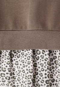 Top tricotat maro cu o textură în dungi, având o fustă suprapusă dintr-un material alb cu pete verzi de leopard.