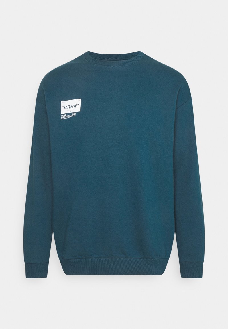 Sudadera de cuello redondo en color teal, hecha de una mezcla de algodón, que presenta una etiqueta blanca en el frente con el texto "CREW" y detalles adicionales de marca.