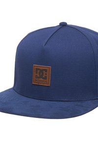 Marineblauwe pet van stof, met een platte rand en een bruine leren patch met het logo. Gladde textuur met een gestructureerd ontwerp.
