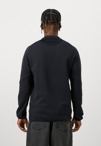 Tamno plavi dukserica s dugim rukavima, rebrastim manžetama i zaobljenim rubom. Glatka tekstura, minimalistički dizajn i bešavne ramena.