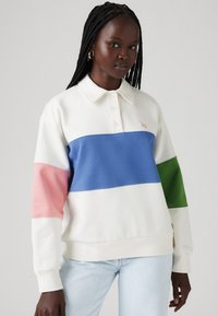 Polaru stila džemperis baltā, zilā, rozā un zaļā krāsu bloku dizainā. Aprīkots ar apkakli, trīs pogu aizdari un ribotām aprocēm.