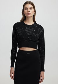 Schwarze, kurz geschnittene Strickjacke mit strukturiertem Design, langen Ärmeln, V-Ausschnitt, Knopfverschluss und figurbetonter Rippkante.