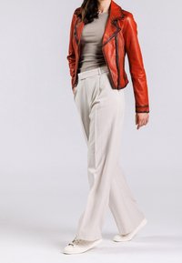 Rode leren motorjasje, beige aansluitend topje, lichtgekleurde brede broek, witte sneakers, gladde textuur en zichtbare ritsdetails.