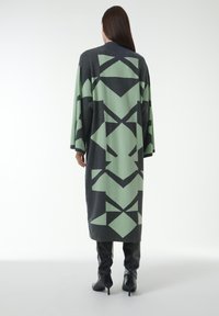 Langes, übergroßes graues und grünes Kleid mit geometrischen Mustern. Hergestellt aus weichem Stoff mit glatter Textur, designed mit weiten Ärmeln.