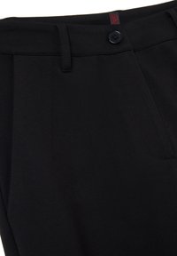 Pantalon noir sur mesure avec une texture lisse, comportant une fermeture à un bouton et des poches avant discrètes. Étiquette rouge à l'intérieur de la ceinture.